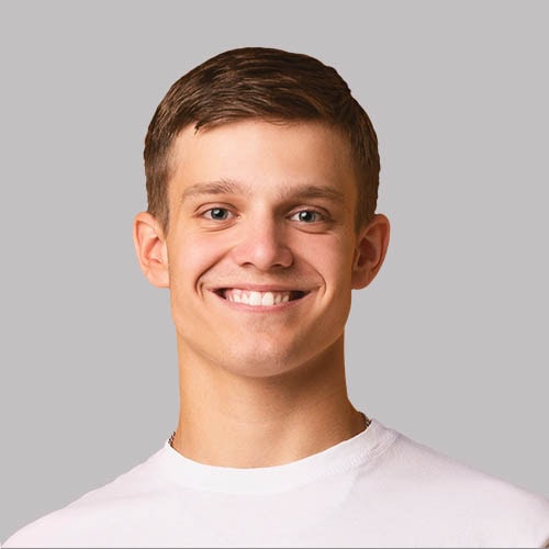 Smiling young man with short brown hair in a white shirt against a gray background.