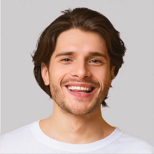 Smiling young man with brown hair and a white shirt on a gray background.