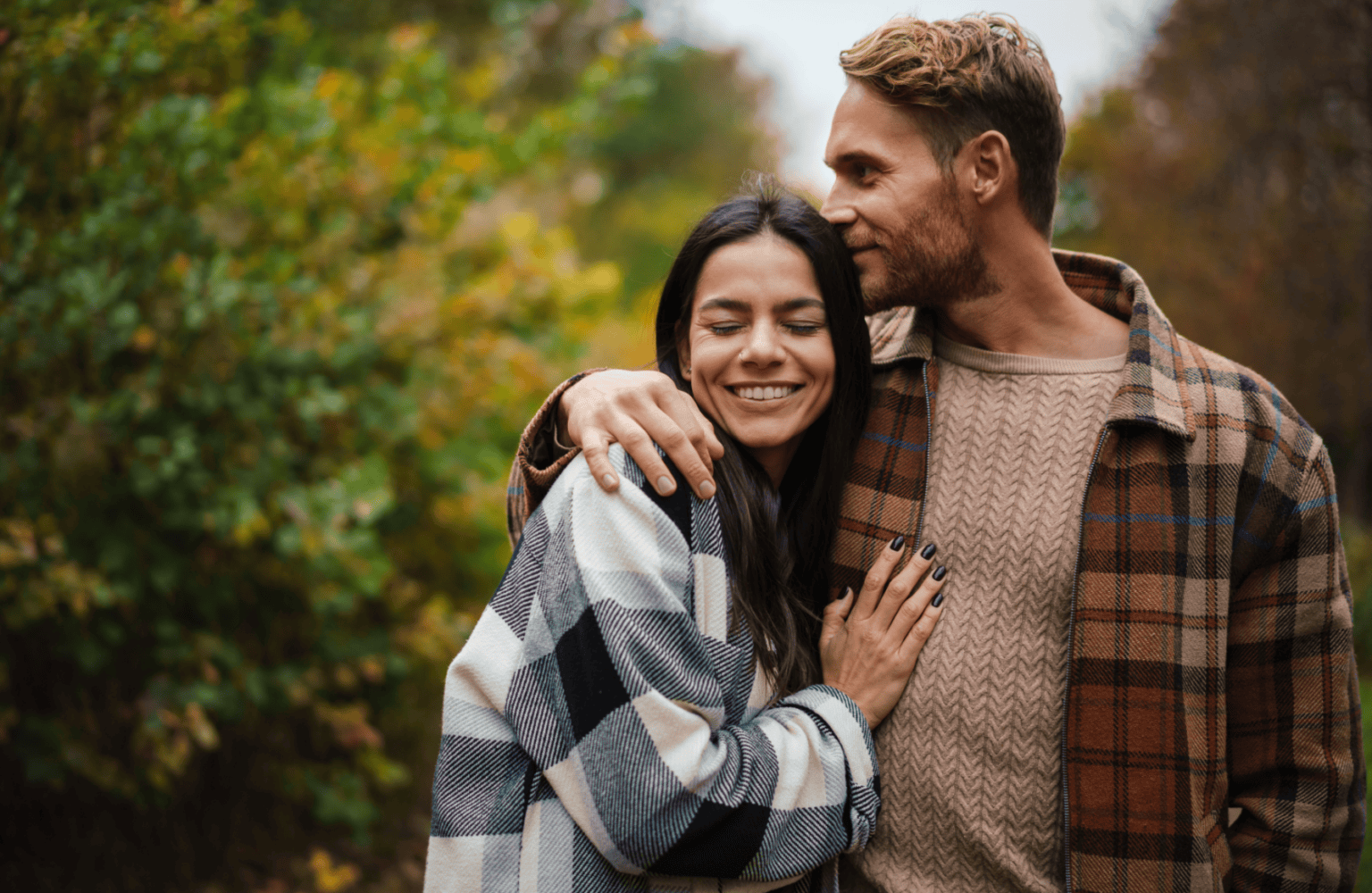 Happy couple embracing outdoors in a park during fall.